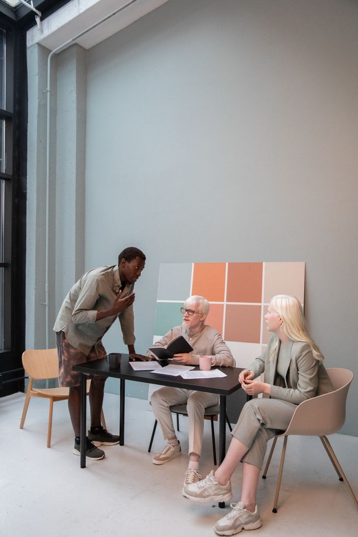 Group of diverse coworkers in stylish outfits gathering around table and discussing details of project in creative workplace