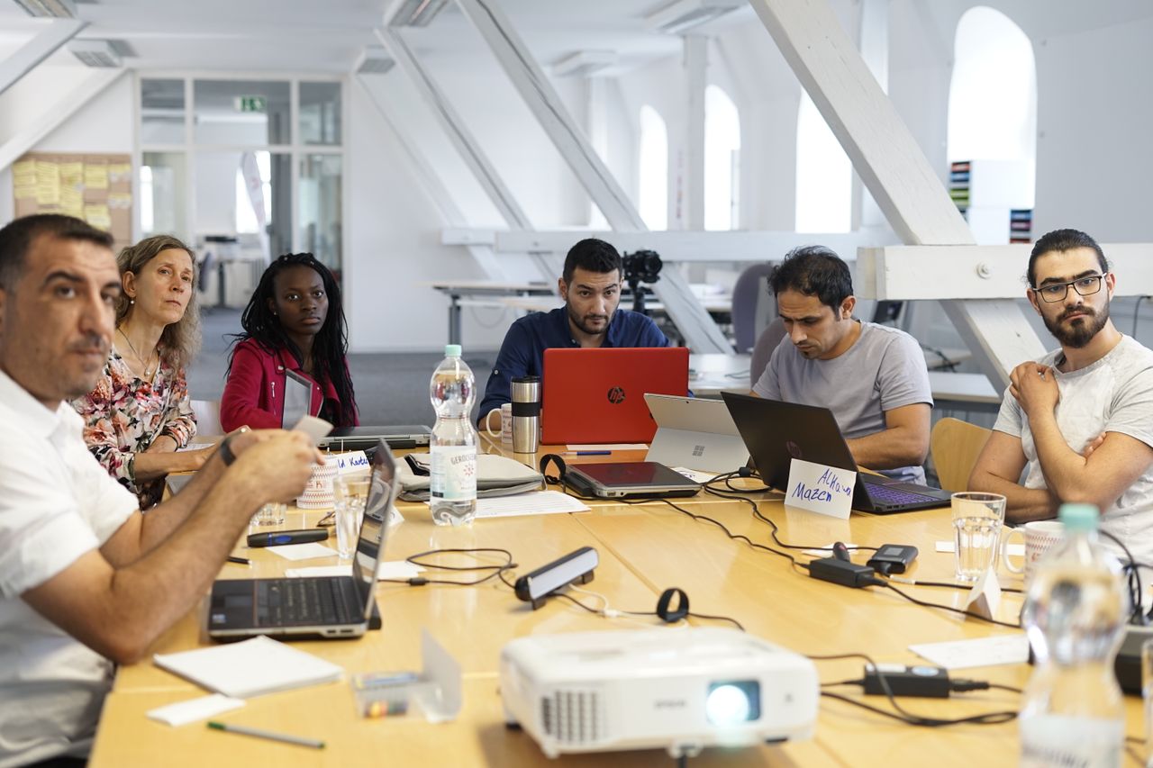 about-01 Diverse team collaborating around a conference table with laptops in a modern office setting.