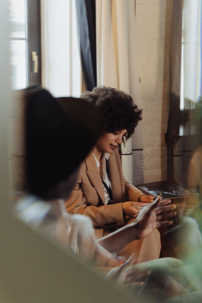 A woman in a brown blazer takes notes during an indoor interview. Soft light and reflection create a moody ambiance.